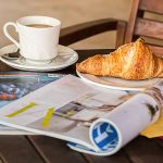 Enjoy a peaceful morning with coffee, croissant, and reading material on a wooden table. — Golden Panda Casino: Ein Blick auf