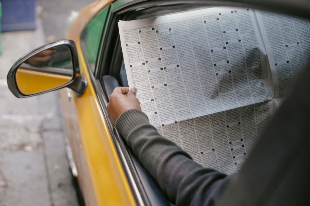 Crop unrecognizable person reading daily newspaper while sitting in car with opened window — test123123