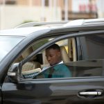 Man reading a newspaper inside his car, parked outdoors during the day. — Unlock Your Winning Edge with BillyBets Login Exper